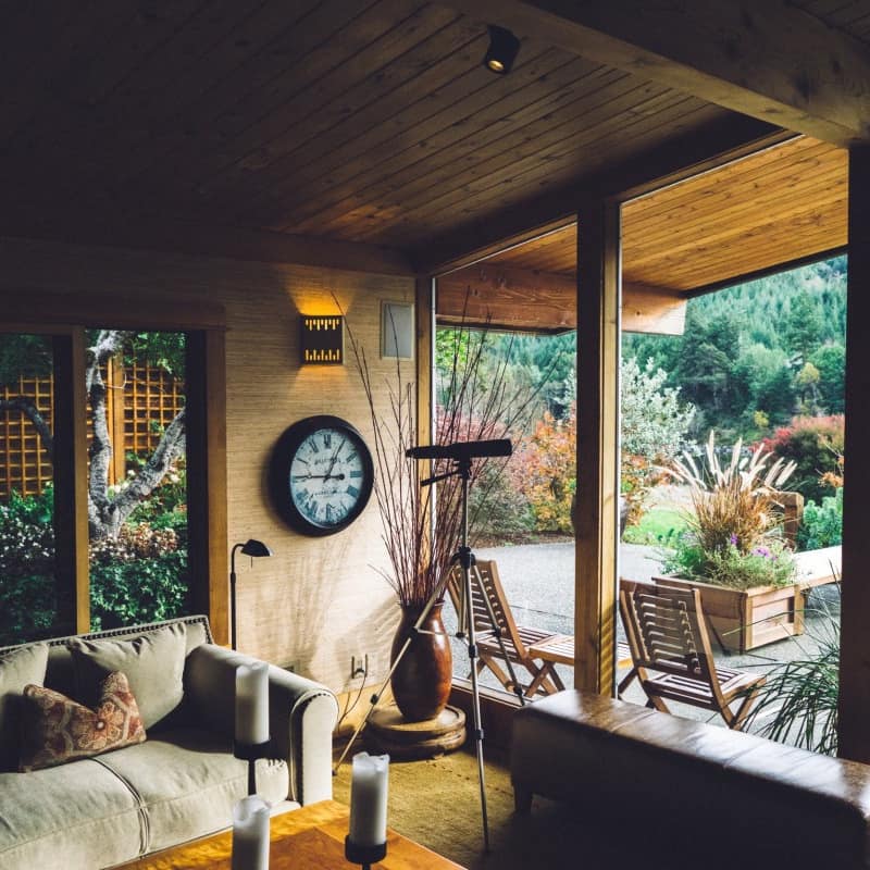 Interior of modern farmhouse with living area, floor-to-ceiling windows, soft cloth sofa with accent pillows and wood ceiling