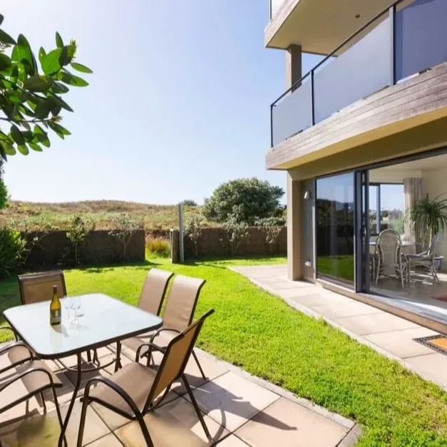 Back patio of a holiday apartment in Tauranga with a table set with wine glasses looking out to green hills on a bright day
