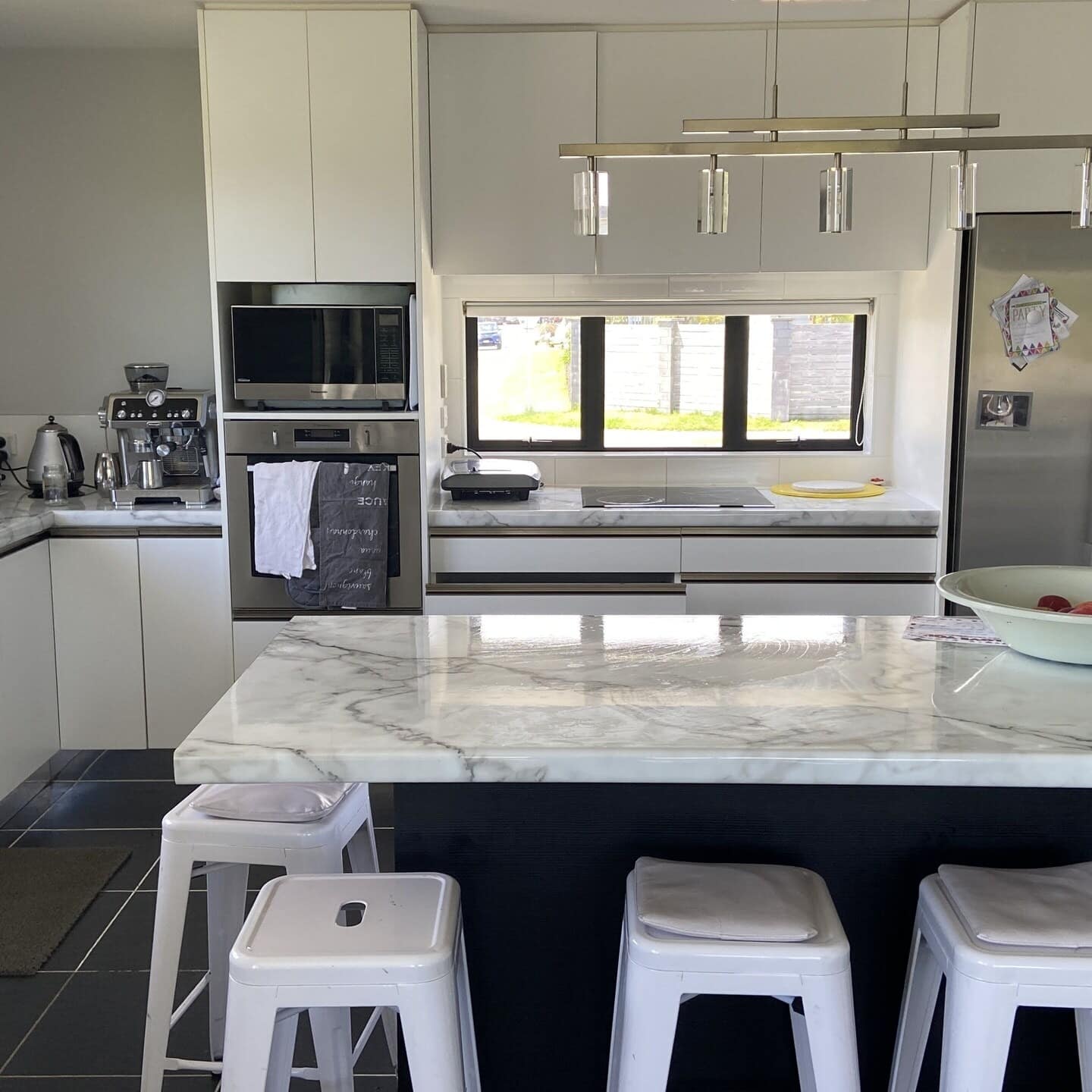 The kitchen of a holiday home complete with appliances with a white marble island surrounded by stools in the foreground